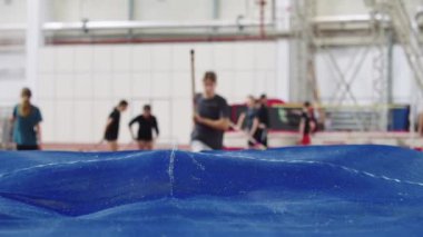 Genç bayan sporcu koşuyor ve kırmızı trambolinde sırıkla atlama yapıyor.