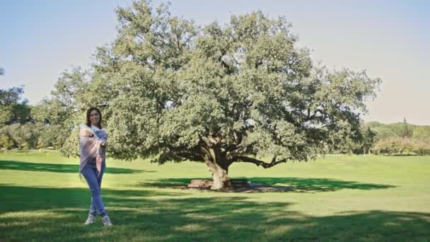 Μια Γυναίκα Στέκεται Μπροστά Από Ένα Μεγάλο Δέντρο Ένα Πάρκο — Αρχείο Βίντεο
