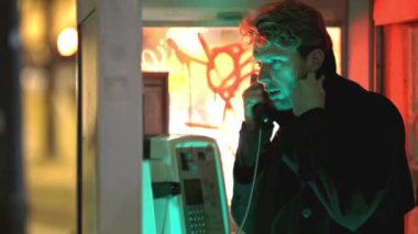 Neon ligth 'teki bir kulübede bir adam telefonla konuşuyor. Kabin loş bir alanda.