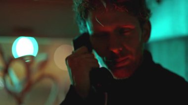 Neon ligth 'te bir adam kara film stili bir telefondan konuşuyor. Görüntüde karanlık ve kasvetli bir atmosfer var. Adamın yüzü telefon ışığıyla aydınlanıyor.