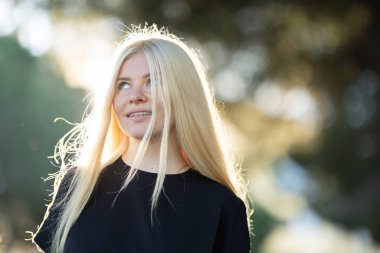 Diş teli ve uzun sarı saçlı genç bir kadın yukarı bakıyor. Yüzünde meraklı ve dikkatli bir ifade var..