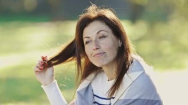 Yetişkin bir kadın gülümsüyor ve gri bir ceket giyiyor. O, çimenli bir alanda duruyor. Mutluluk ve rahatlama kavramı