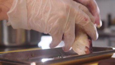 Beyaz eldiven giyen bir kişi, bir barda ya da restoran ortamında deniz ürünleri, ahtapot hazırlarken görülüyor. Bireyler malzemelerle çalıştıkça aşçılık görevlerine odaklanırlar..