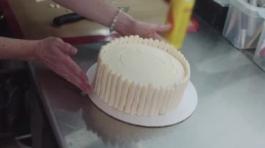 Bir insan pastayı ustalıkla beyaz krema ile süsler, güzel bir tasarım yaratmak için titizlikle yayar ve yumuşatır..