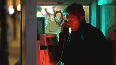 Şık bir adam, Neon ligth 'teki kabinde siyah bir telefon kulübesinde konuşuyor. Görüntüde karanlık ve kasvetli bir atmosfer var. Adamın yüzü telefon ışığıyla aydınlanıyor.