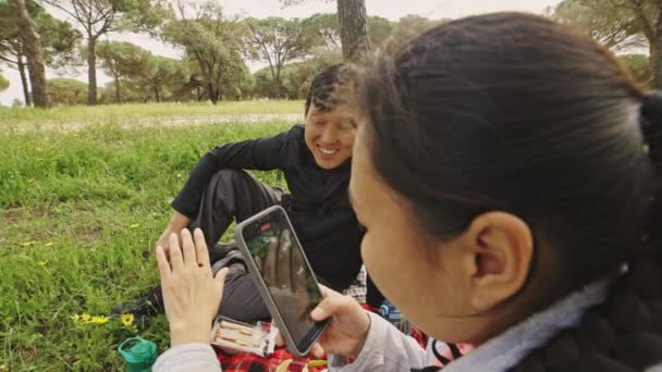 女性が草の上に座って ラビを捕まえるためにスマートフォンを使用しています 彼女は携帯を見ている — ストック動画
