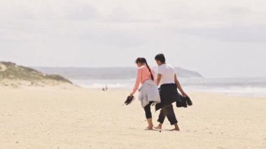 Arka planda bulutlu bir gökyüzü olan plajda yürüyen bir çift.