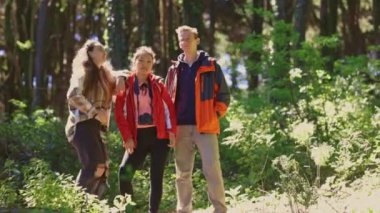 Üç kişi ormanda dikiliyor, biri kırmızı ceket giyiyor. Sahne huzurlu ve huzurlu, çünkü bir grup insan doğayla çevrili.