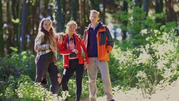3人が森に立って 写真を撮っている 男性は赤いジャケットを着ていて 女性は黒いジャケットを着ています 女性は彼女の手に携帯電話を握っている — ストック動画