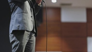 Takım elbise ve kravat takmış bir adam mikrofonun önünde duruyor. Profesyonel ve resmiyet kavramı, büyük olasılıkla halka açık bir konuşma ya da performansa hazırlanıyor.
