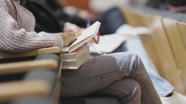 ある女性が教室で膝に本を持って座っている 彼女はノートに書いている — ストック動画