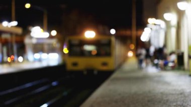 Bir tren istasyonunun bulanık bir görüntüsü. Etrafta birkaç kişi var. Sahne biraz gizemli ve biraz da uğursuzdur.