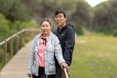 Bir adam ve bir kadın, siyah ceketli bir adam ve pembe gömlekli bir kadınla ahşap bir köprüde duruyorlar.