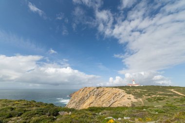 Uzakta deniz feneri olan güzel bir okyanus manzarası. Gökyüzü açık ve su sakin.