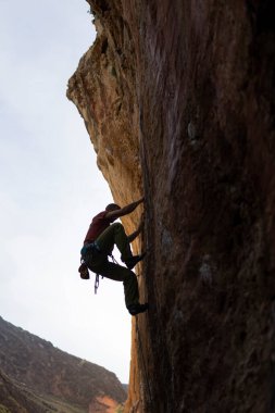 Mağaradaki kaya duvarına tırmanan bir insan. Mağara karanlık ve sahnedeki tek kişi o.