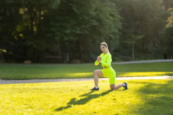 一个穿着霓虹灯绿色衣服的女人正在草地上做瑜伽姿势 她衣服的鲜艳色彩和茂盛的绿草营造出一种愉快而充满活力的气氛 — 图库照片