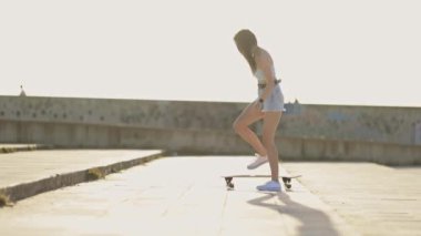 Bir kadın kaldırımda kaykay yapıyor. O, şort ve bir kolsuz bluz giyiyor. Görüntünün rahat ve rahat bir havası var.