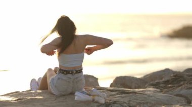 Bir kadın okyanus kıyısındaki bir kayanın üzerinde oturuyor, saçını tarıyor. Sahne sakin ve sakin. Arka planda dalgaların sesi var.