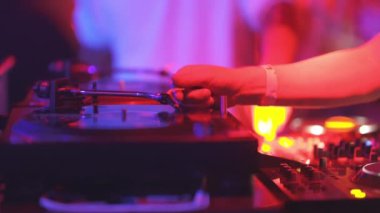 Bir kişi kırmızı arka planlı bir pikabı çalıyor. Sahne enerjik ve canlı, çünkü kişi aktif olarak müzik çalmakla meşgul.