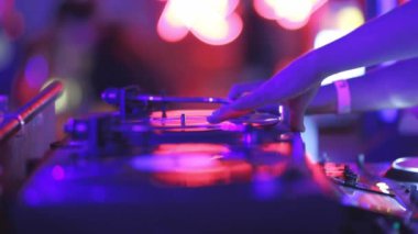 Bir kişi mor arka planı olan bir pikabı çalıyor. Müzik yüksek ve ışıklar parlak.