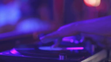 Bir kişi mor arka planı olan bir pikabı çalıyor. Sahne enerjik ve canlı, kişinin müzikle aktif olarak ilgilenmesi gibi.