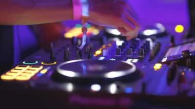 Bir kişi mor arkaplanlı bir DJ seti çalıyor. DJ setinde bir sürü düğme ve düğme var ve kişi bir düğmeye basıyor.
