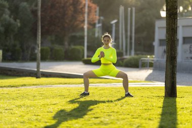 Neon sarısı kıyafetli bir kadın parkta yoga pozu veriyor. Enerji ve pozitiflik kavramı, kadın antrenmanına ve açık havanın tadını çıkarmaya odaklanmış.