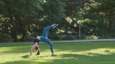 Bir kadın çimenli bir alanda amuda kalkıyor. Özgürlük ve güç kavramı, kadın açık bir alanda zorlu bir yoga pozisyonu sergiliyor. Parlak yeşil çimenler