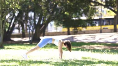 Bir kadın çimenli bir alanda şınav çekiyor. Kadın doğa ve çimen tarlasıyla çevrili olduğu için, görüntü huzurlu ve huzurlu bir ruh haline sahip.