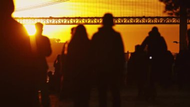 Bir grup birey köprünün yanında durup Tagus Nehri 'ndeki feribotu izliyor..