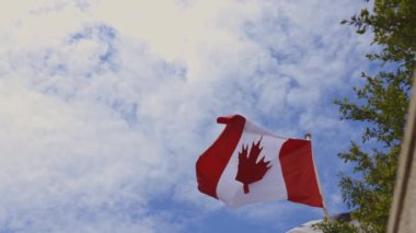 Gökyüzünde bir akçaağaç yaprağı dalgalanan bir Kanada bayrağı. Gökyüzü mavi ve bazı bulutlar var.