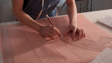 Bir kadın bir kağıt parçasına şablon çiziyor. Kalem ve cetvel kullanıyor.