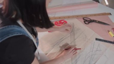 Bir kadın bir kağıt parçasına tasarım çiziyor. Tasarımı kesmek için bir cetvel ve makas kullanıyor.