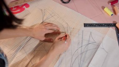 Bir insan bir kağıt parçasına elbise çiziyor. Elbise, kırmızı bukleli uzun, dalgalı bir elbisedir. Tasarımı yaratmak için bir kalem ve cetvel kullanıyor.