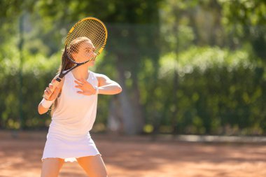 Bir kadın kortta tenis oynuyor. Beyaz bir elbise giyiyor ve elinde bir tenis raketi tutuyor.