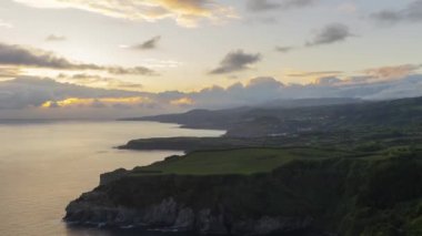 Azores - San Miguel Adası - güzel bir okyanus manzarası ve bulutlu bir gökyüzü olan bir yamaç. Gökyüzü mavi ve turuncu renklerin karışımıdır. Huzurlu ve huzurlu bir atmosfer yaratır.