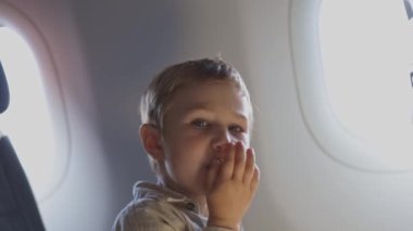 Küçük bir çocuk bir uçağın penceresinden dışarı bakıyor. Çocuk elinde bir aperatif tutuyor.