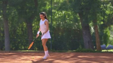Bir kadın kortta tenis oynuyor. Elinde tenis raketi ve tenis topu tutuyor.