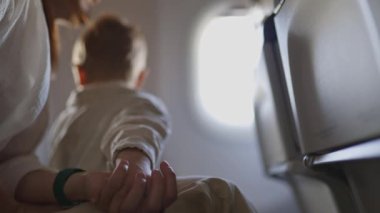 Bir kadın ve bir çocuk uçakta oturuyorlar. Çocuk pencereden dışarı bakmaktadır. Kadın çocuğun elini tutuyor.