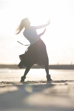 Sahilde etekli bir kadın dans ediyor. Özgürlük ve neşe kavramı, kadın tamamen dansla meşgul ve o da eğleniyor. Plaj manzarası genel rahatlama havasına katkı sağlıyor.