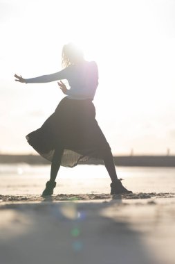 Sahilde etekli bir kadın dans ediyor. Görüntünün neşeli ve neşeli bir havası var. Kadın güneşin altında dans ediyor ve kumsal manzarası parlak ve neşeli.