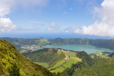 Güzel bir göl manzarası ve berrak mavi gökyüzü olan dağlar. Göl yeşil tepeler ve ağaçlarla çevrili.