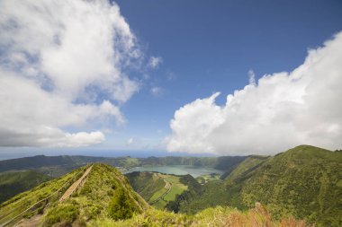 Uzakta gölü olan bir dağın tepesi. Gökyüzü birkaç bulutla daha açık.