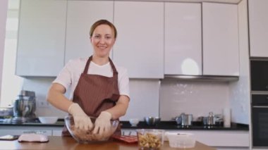 Bir kadın mutfakta beyaz bir fırın ve siyah bir tezgahla yemek pişiriyor. Önlük ve eldiven giyiyor.