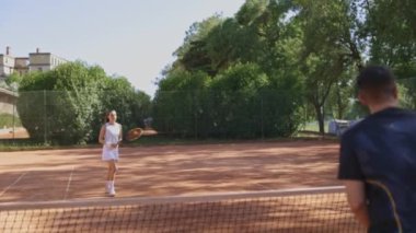 Bir adam ve bir kadın kortta tenis oynuyorlar, geniş açılı.