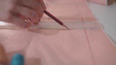 Bir kadın eli pembe bir yüzeye bir kalem ve cetvelle düz bir çizgi çiziyor..