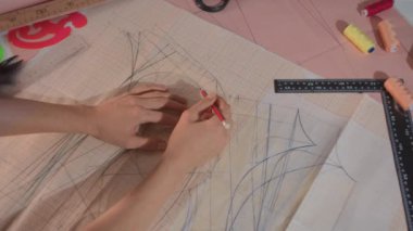 Bir kadın eli, bir kalem ve cetvel kullanarak büyük bir kağıt yaprağına desen çizer gibi görünür..