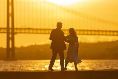 Gün batımında köprünün önünde bir çift dans ediyor. Batan güneşin altın ışığı çiftin siluetini oluşturur..