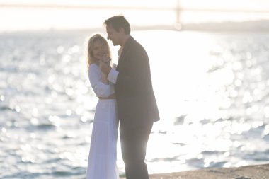 Bir erkek ve kadın gün batımında kumsalda birlikte dans ediyorlar, su altın ışığı yansıtıyor..