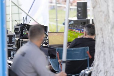 Futbol televizyonu yapan iki işçi parkta futbol maçı seyrediyor.